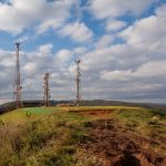 Torres de telecomunicações instaladas no alto de uma colina coberta por vegetação, sob céu nublado em Minas Gerais.