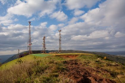 Torres de telecomunicações instaladas no alto de uma colina coberta por vegetação, sob céu nublado em Minas Gerais.