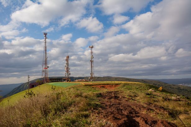 Torres de telecomunicações instaladas no alto de uma colina coberta por vegetação, sob céu nublado em Minas Gerais.