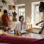 Grupo diverso de mulheres colaborando em um estúdio de design de moda equipado com máquinas de costura