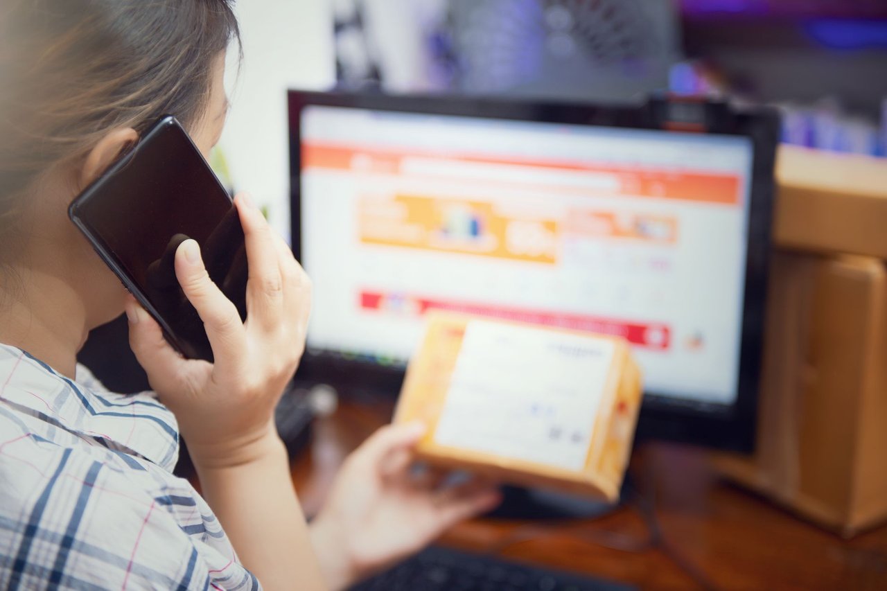 Mulher usa o celular enquanto verifica uma encomenda recebida em casa.