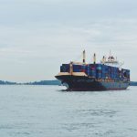Navio cargueiro transportando contêineres pelo mar, em referência ao comércio internacional.
